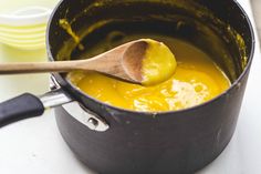 a wooden spoon in a black pot filled with yellow liquid next to plates and bowls