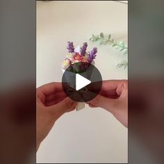 a person holding a small vase with flowers in it's palm and the video is playing