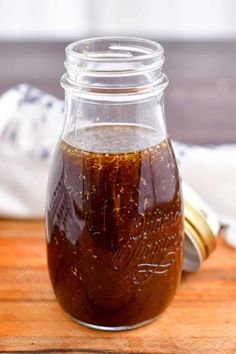 a jar filled with brown liquid sitting on top of a wooden table next to a spoon