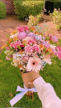 a bouquet of flowers is being held by someone's hand in front of some bushes