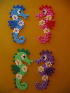 four seahorses made out of perler beads on a yellow surface with white and blue flowers