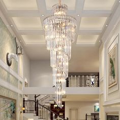 a chandelier hanging from the ceiling in a living room with stairs and paintings on the walls