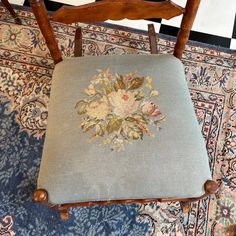 a chair with a floral embroidered seat pad on top of carpeted floor next to rug