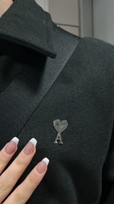 a woman's manicured nails with a silver heart pin on her lapel