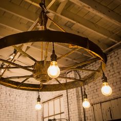 several light bulbs are hanging from a circular chandelier in an old warehouse setting