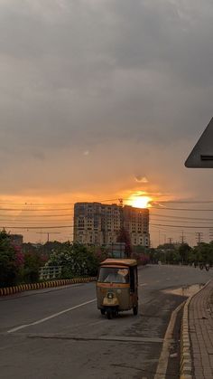 the sun is setting over a street with cars on it and buildings in the background