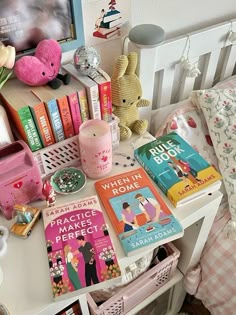 a white table topped with lots of books next to a pink teddy bear and lamp