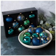 a bowl filled with blue and green christmas ornaments next to a black box on a table