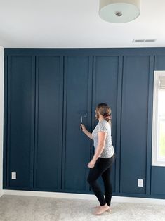 a woman standing in front of a blue wall holding a paint roller and painting the walls