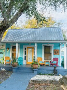 a blue and white house with two chairs on the front porch next to a tree