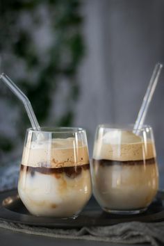 two glasses filled with liquid sitting on top of a table next to each other and straws sticking out of them