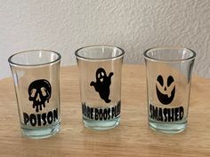 three shot glasses sitting on top of a wooden table next to each other with the words halloween printed on them