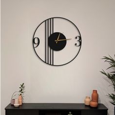 a black clock on the wall above a table with vases and potted plants