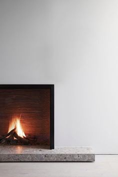 a fireplace that is lit up in the middle of a room with white walls and flooring