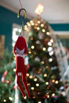 an elf hanging from a string in front of a christmas tree