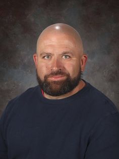 a man with a bald head and blue sweater posing for a photo in front of a dark background