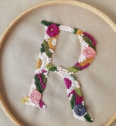 the letter q is made up of flowers and leaves in an embroidery pattern on a wooden hoop