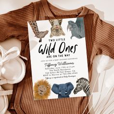 two little wild ones are on the way sign next to baby shoes and stuffed animals