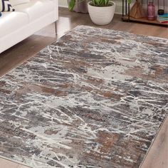 a large area rug with an abstract design in grey, brown and white colors on a wooden floor