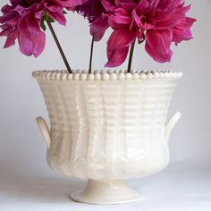 purple flowers are in a white vase on a table