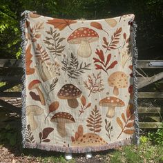 a blanket with mushrooms and leaves on it hanging from a wooden fence in the woods