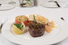 a white plate topped with meat, shrimp and lemon wedges on top of a table