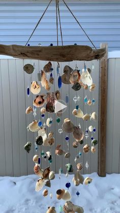 a wind chime made out of seashells hanging from a wooden beam in the snow