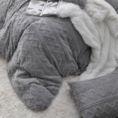 an unmade bed with grey and white comforter on it's side, next to two pillows