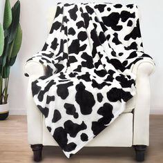 a black and white cow print blanket sitting on top of a chair next to a potted plant