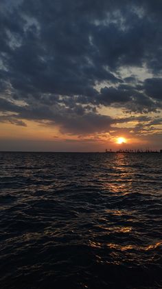 the sun is setting over the ocean as it reflects in the water with dark clouds