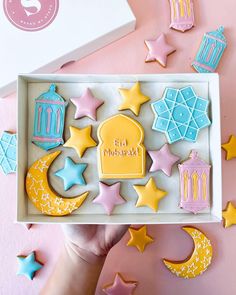 a box filled with decorated cookies on top of a pink table next to stars and crescents