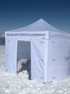 a white tent sitting in the middle of snow covered ground with an advertisement on it