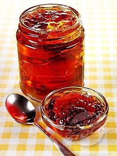 there is a jar of jam and two spoons on the table with yellow checkered cloth