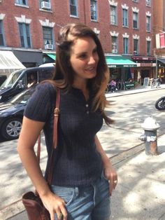 a woman is standing on the sidewalk with her purse in hand and looking at the camera