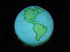 a blue and green cake with the world on it's side, sitting on a black surface