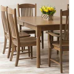 a wooden dining table with chairs and a vase filled with yellow tulips on top