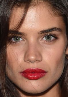 a close up of a woman with red lipstick on her face and long dark hair