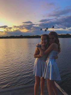 two girls hugging each other while standing on a boat in the water at sunset or dawn