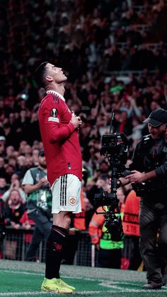 a man standing on top of a soccer field next to a cameraman in front of a crowd