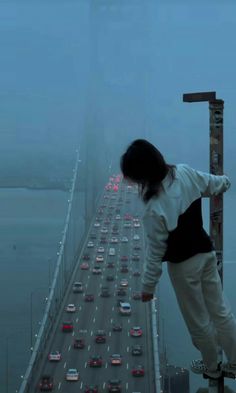 a skateboarder is standing on the edge of a tall bridge with traffic in the background