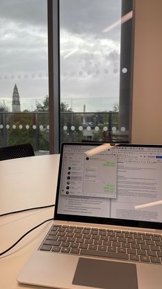 an open laptop computer sitting on top of a white table in front of a window