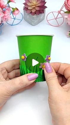 two hands holding up a green cup with flowers on the top and an arrow in the middle