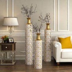 three tall vases with branches in them on a wooden floor next to a white couch