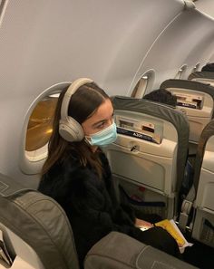 a woman with headphones and a face mask sitting on an airplane seat looking at the camera