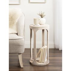 a small table with books and a cup on it in front of a white chair