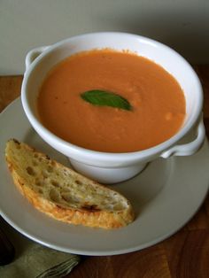 a white plate topped with a bowl of soup and a piece of bread