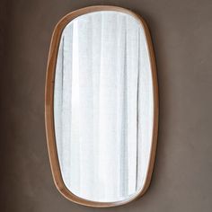 an oval mirror hanging on the wall in front of a white and brown striped curtain