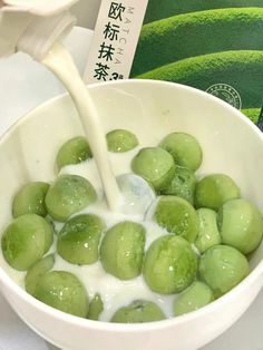 a white bowl filled with green grapes and milk being poured into it by a spoon