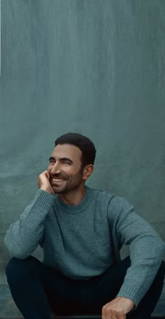 a man sitting on the ground with his hand under his chin and smiling at the camera