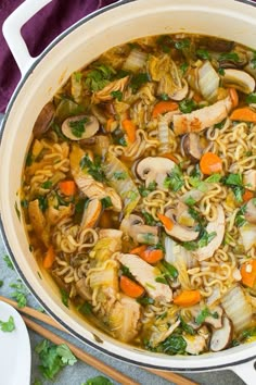 a pot filled with noodles and vegetables on top of a purple cloth next to chopsticks